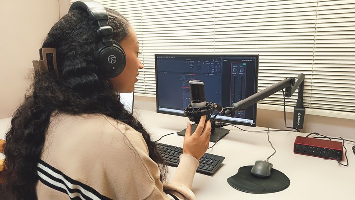 A person with a hand at the microphone in front of the Podcast Room A workstation