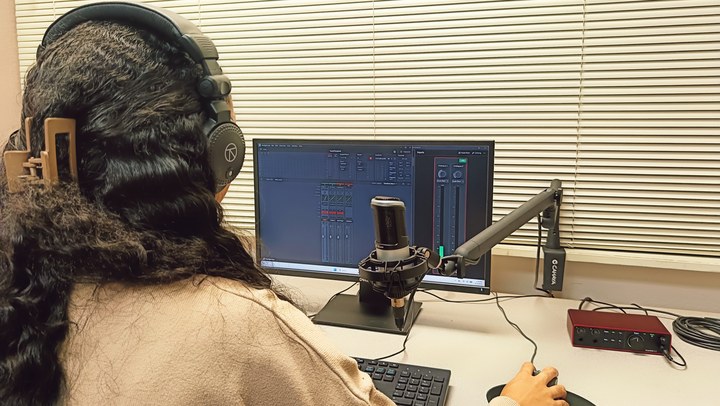 A view from behind the headphones toward the monitor and microphone in Podcast Room A