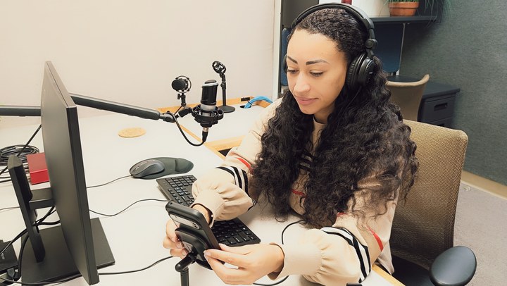 A person placing a phone on a desktop stand in Podcast Room A