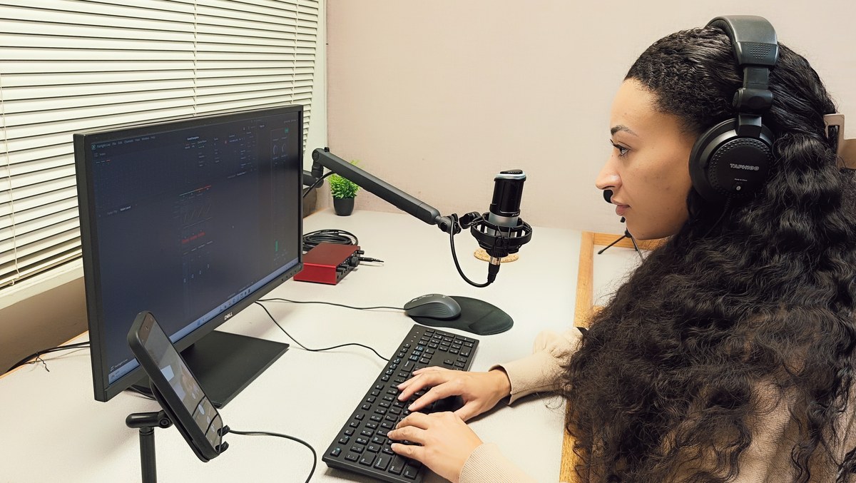 A person wearing headphones and using the keyboard beside a microphone in Podcast Room A