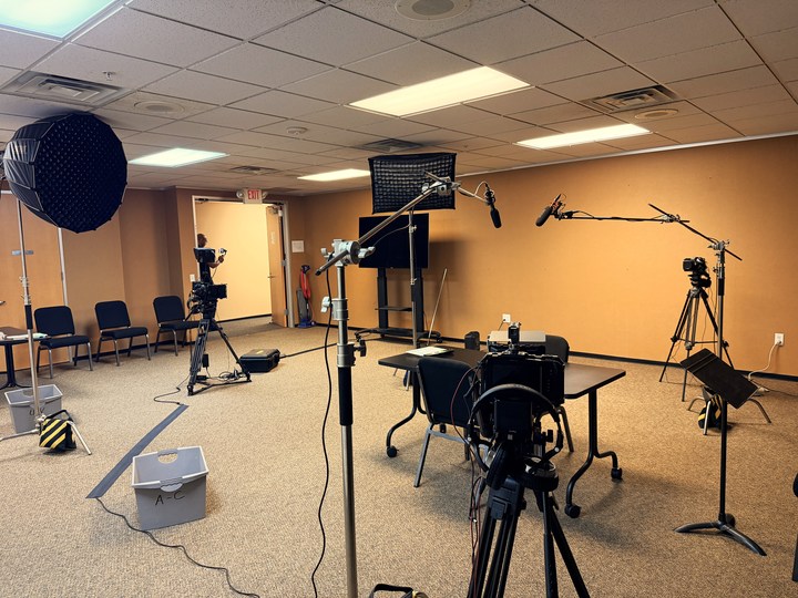 Cameras, boom microphones and lights arranged around a rehearsal table
